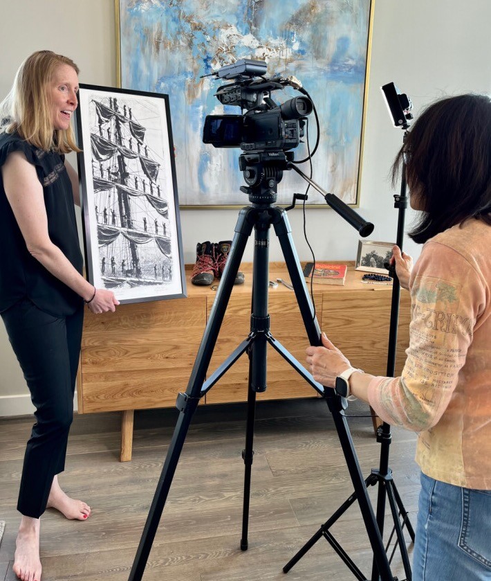 Heather Nickerson standing in front of a TV camera talking about a piece of artworks she's holding