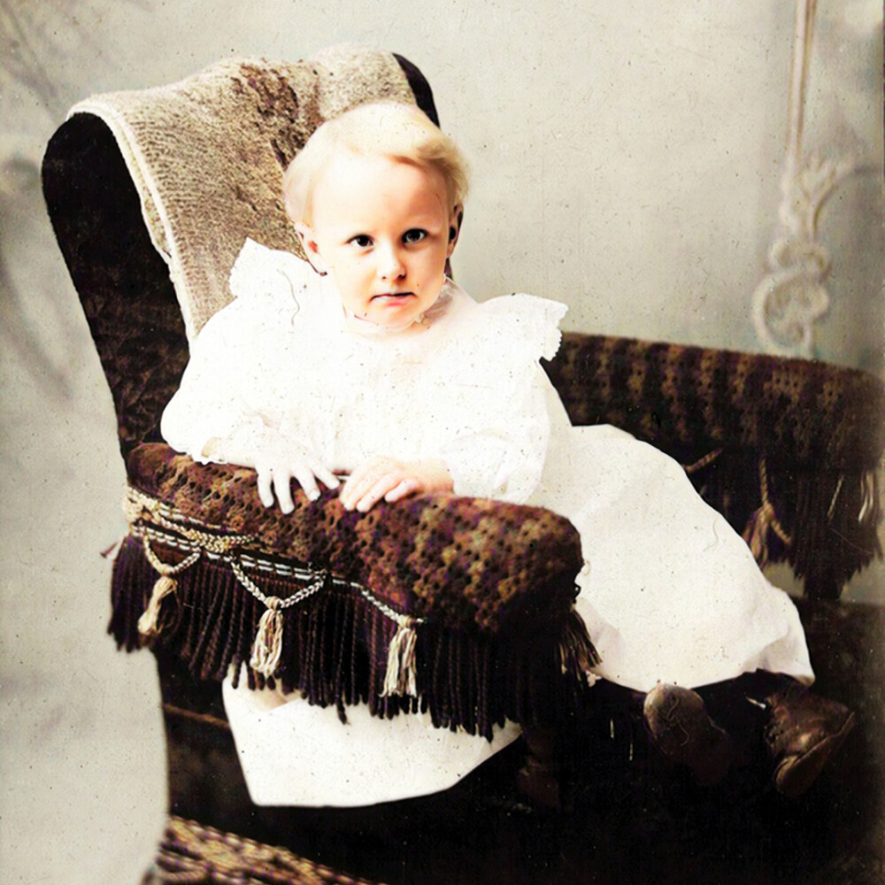 Old fashioned black and white photo of a child in a long gone on a chair circa 1897